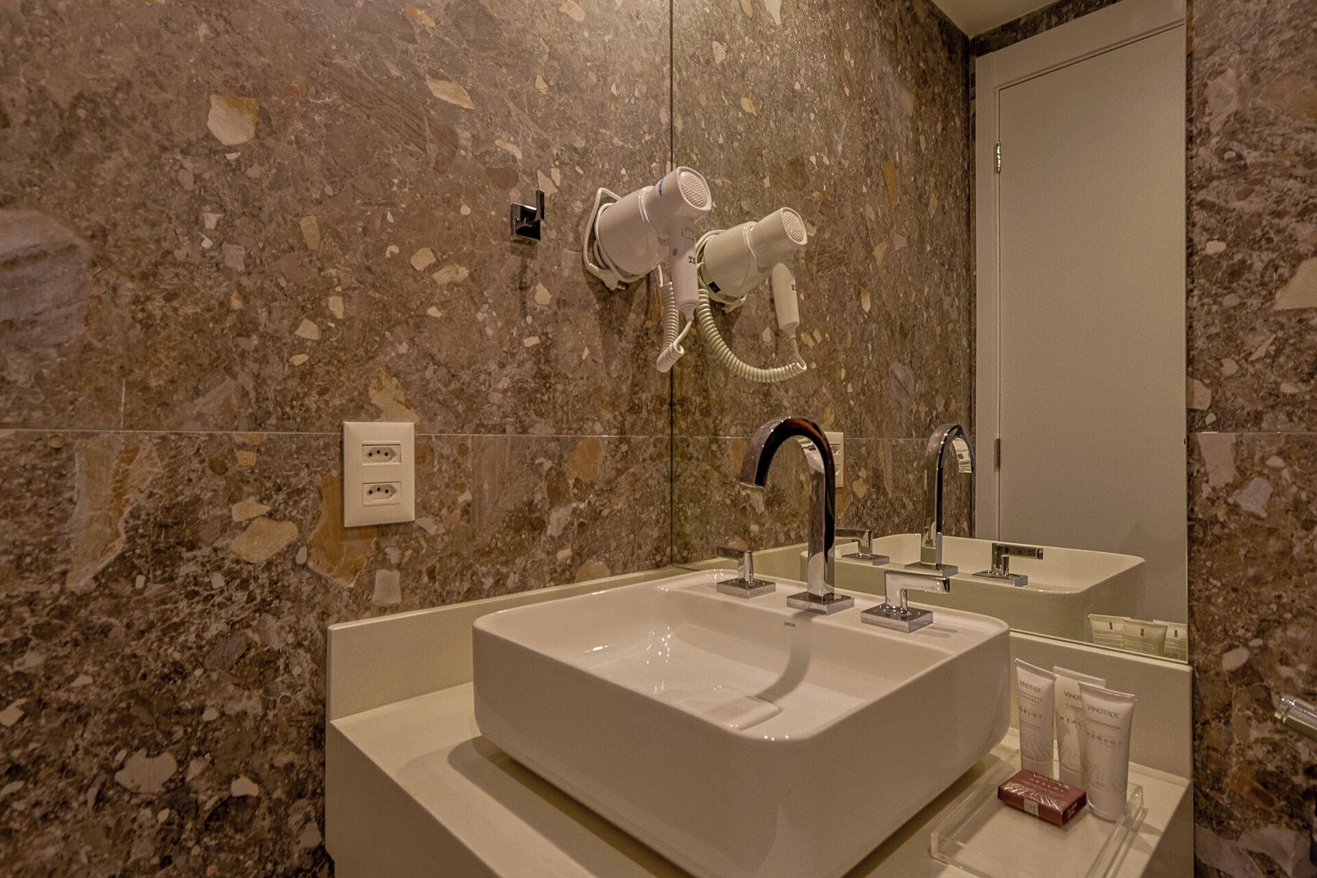 Un baño con un lavamanos grande, un espejo y un secador de pelo fijado en la pared.