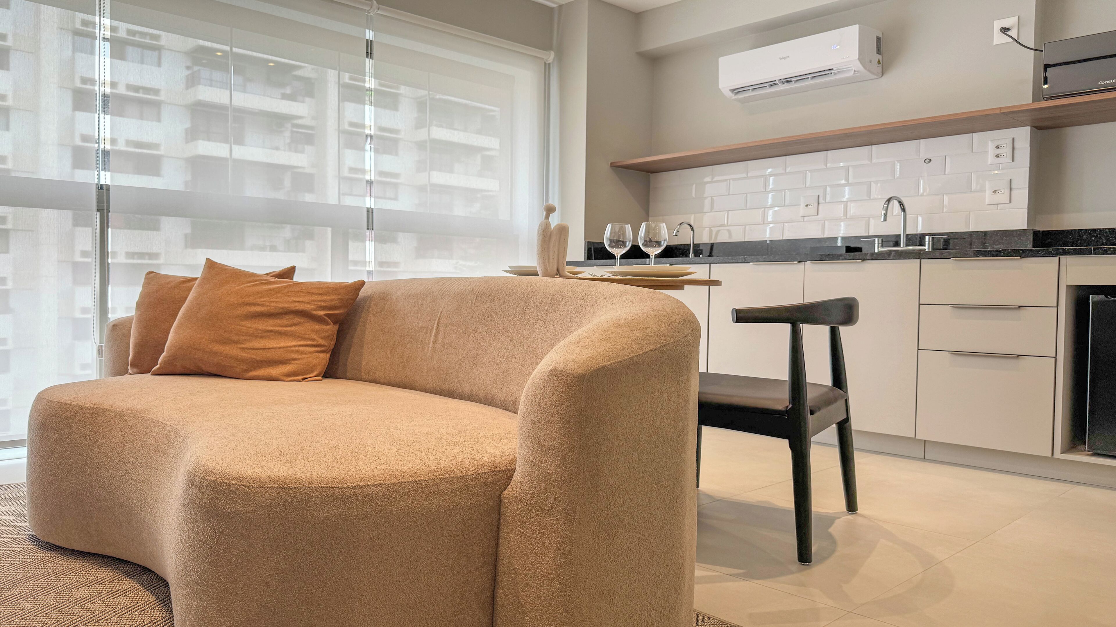 Una sala de estar moderna con un sofá beige, una mesa de comedor con sillas y una cocina con armarios blancos y un equipo de aire acondicionado.