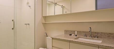 Une salle de bain moderne dotée d’une douche à parois de verre, de toilettes, d’un lavabo avec un plan de travail en granit et d’un miroir au-dessus du lavabo.