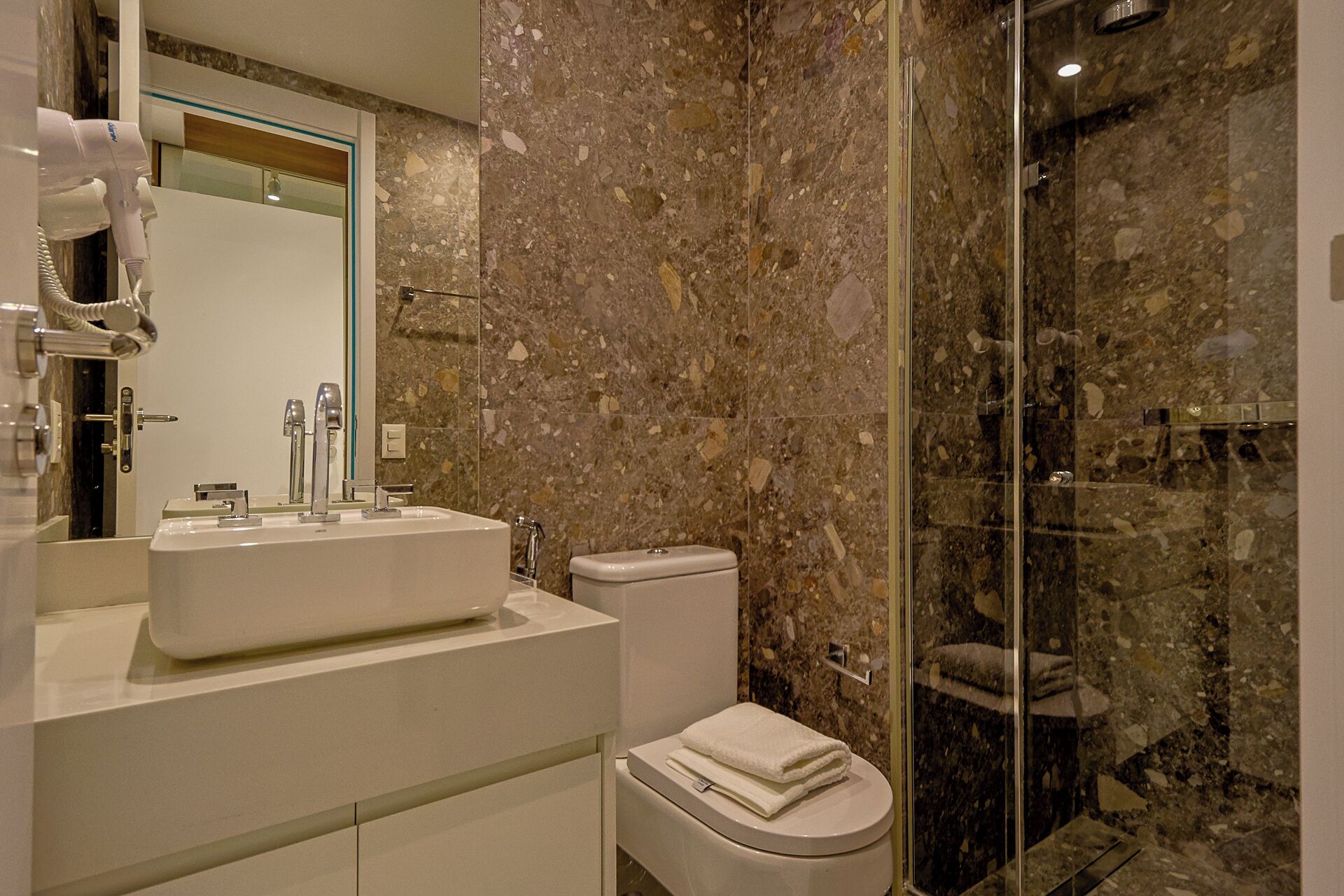 Baño con pared de mármol, lavabo, inodoro y cabina de ducha de vidrio.