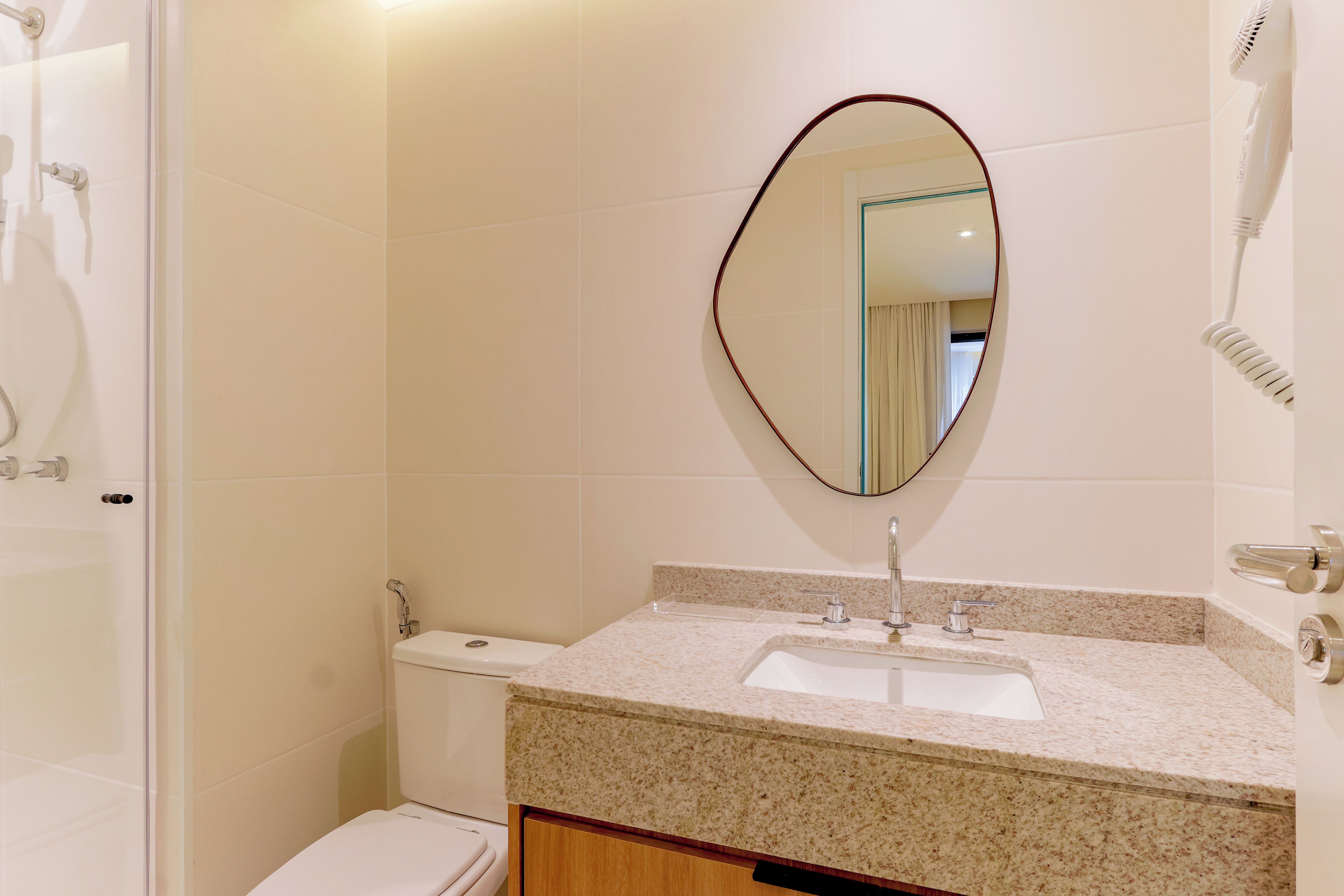Un baño con inodoro blanco, lavamanos con encimera de granito, espejo con marco rojo y secador de pelo en la pared.