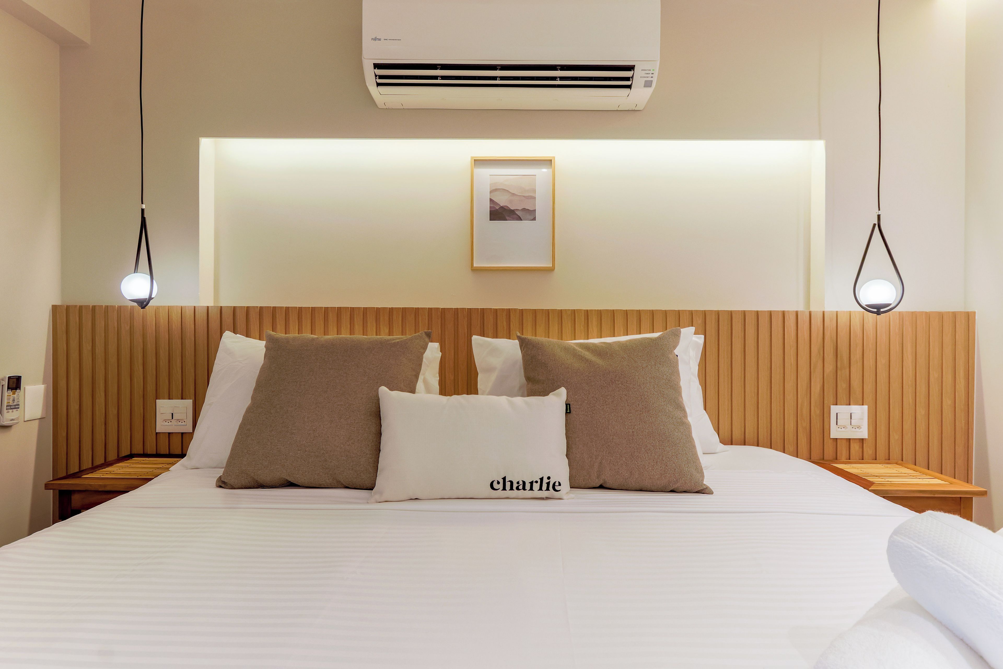 A hotel room with a bed, a framed picture on the wall, and an air conditioning unit above the bed.