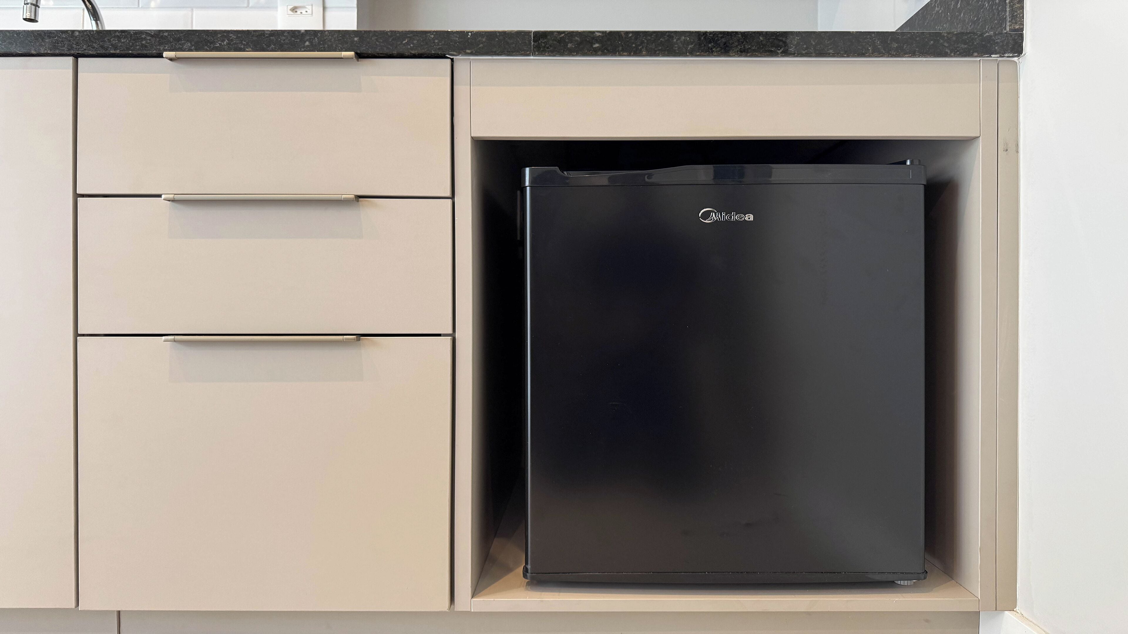Una cocina con un refrigerador negro, armarios color beige y una encimera negra.