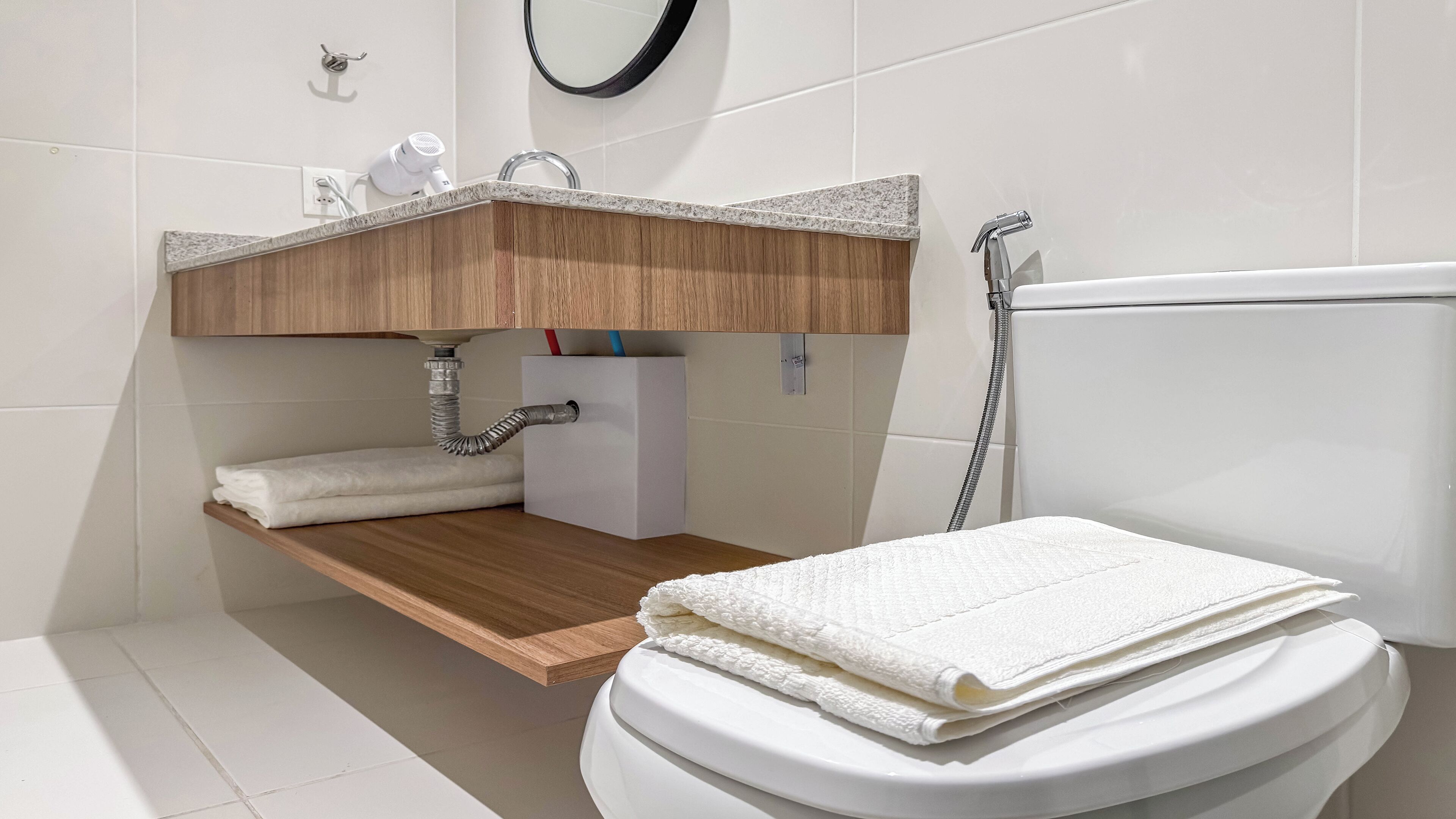 A modern bathroom with a white toilet, a wooden vanity with a sink, and a towel rack.