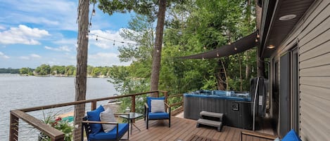 A deck with outdoor furniture, a hot tub, and a view of a lake.