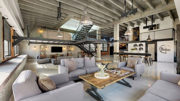 Un loft spacieux avec un plafond haut, des poutres apparentes, un escalier, un coin bar et un grand téléviseur à écran plat.