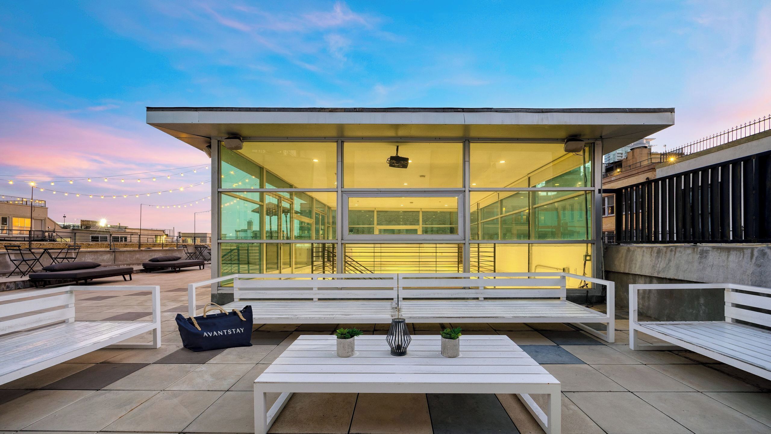 A modern outdoor seating area with white benches, a table, and a bag labeled 'AVANTSTAY.'