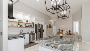 Una cocina moderna con una isla de mármol, electrodomésticos de acero inoxidable y una lámpara de techo geométrica.