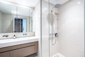 A modern bathroom with a glass-enclosed shower, a large mirror, and a white vanity with a marble countertop. - Pure Voyage Beachfront  (Dubai)