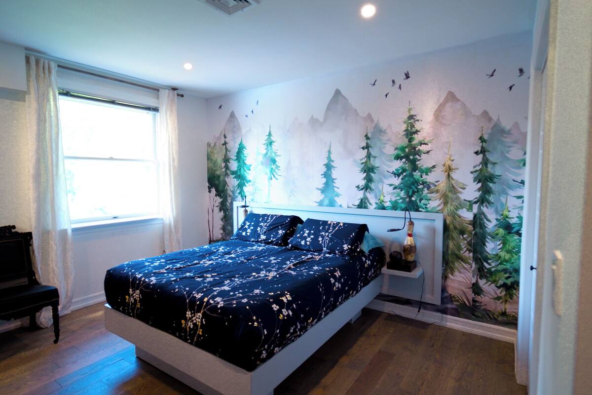 A bedroom with a bed, a nightstand, a window, and a wall mural.