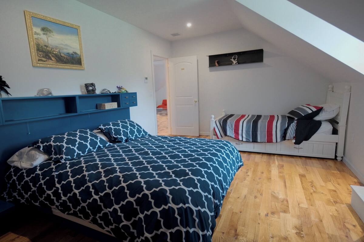 A bedroom with a bed, a dresser, a painting on the wall, and a door leading to another room.