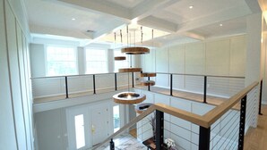 Un intérieur spacieux avec un plafond haut, un escalier doté d’une rampe en bois et un luminaire suspendu.