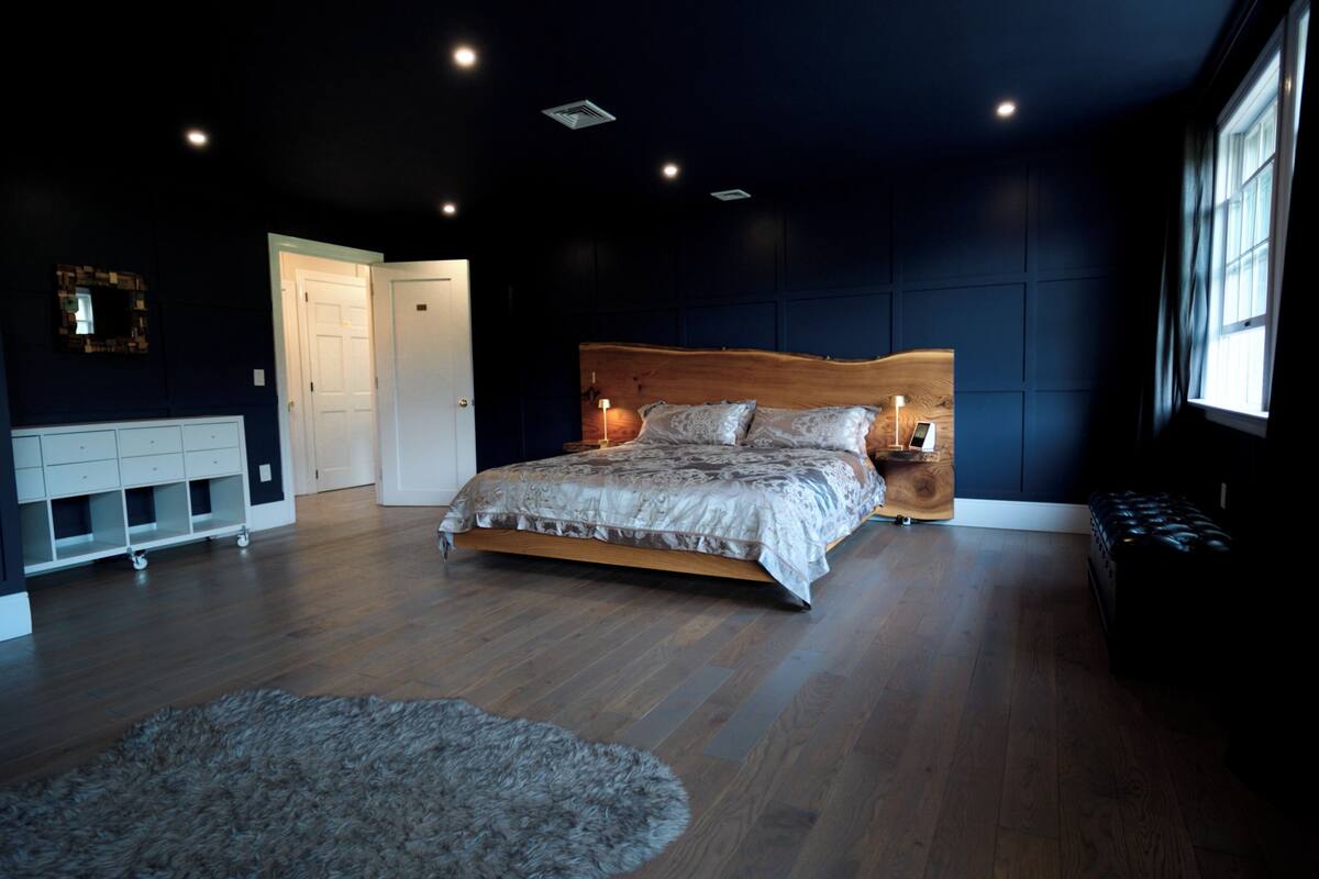 A bedroom with a wooden bed, a white dresser, a fluffy rug, and a large window.