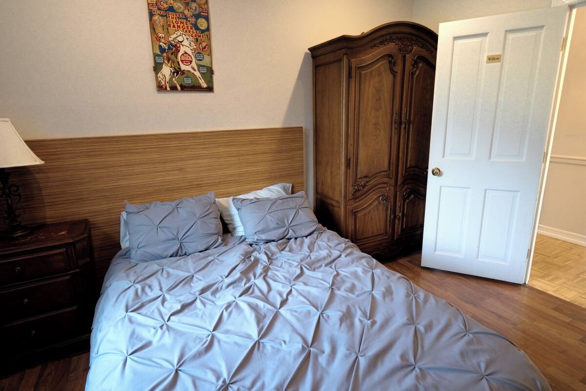 A bedroom with a bed, a nightstand, a lamp, a wardrobe, and a door.