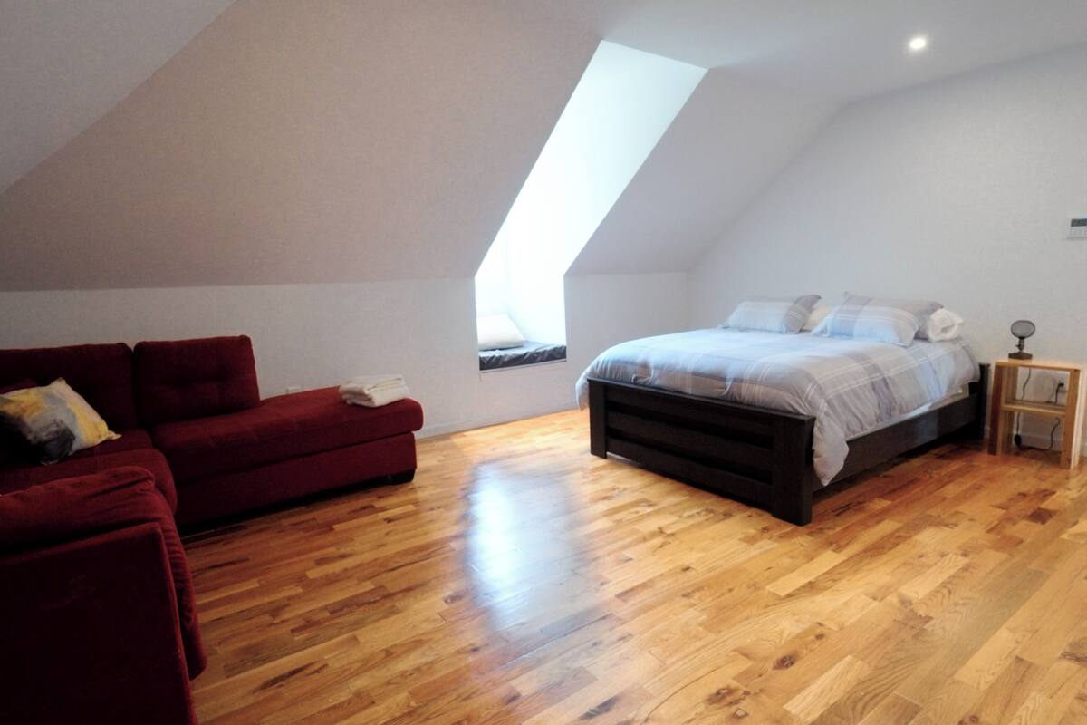 A bedroom with a sloped ceiling, a bed with a headboard, a red sofa, and a small bedside table.