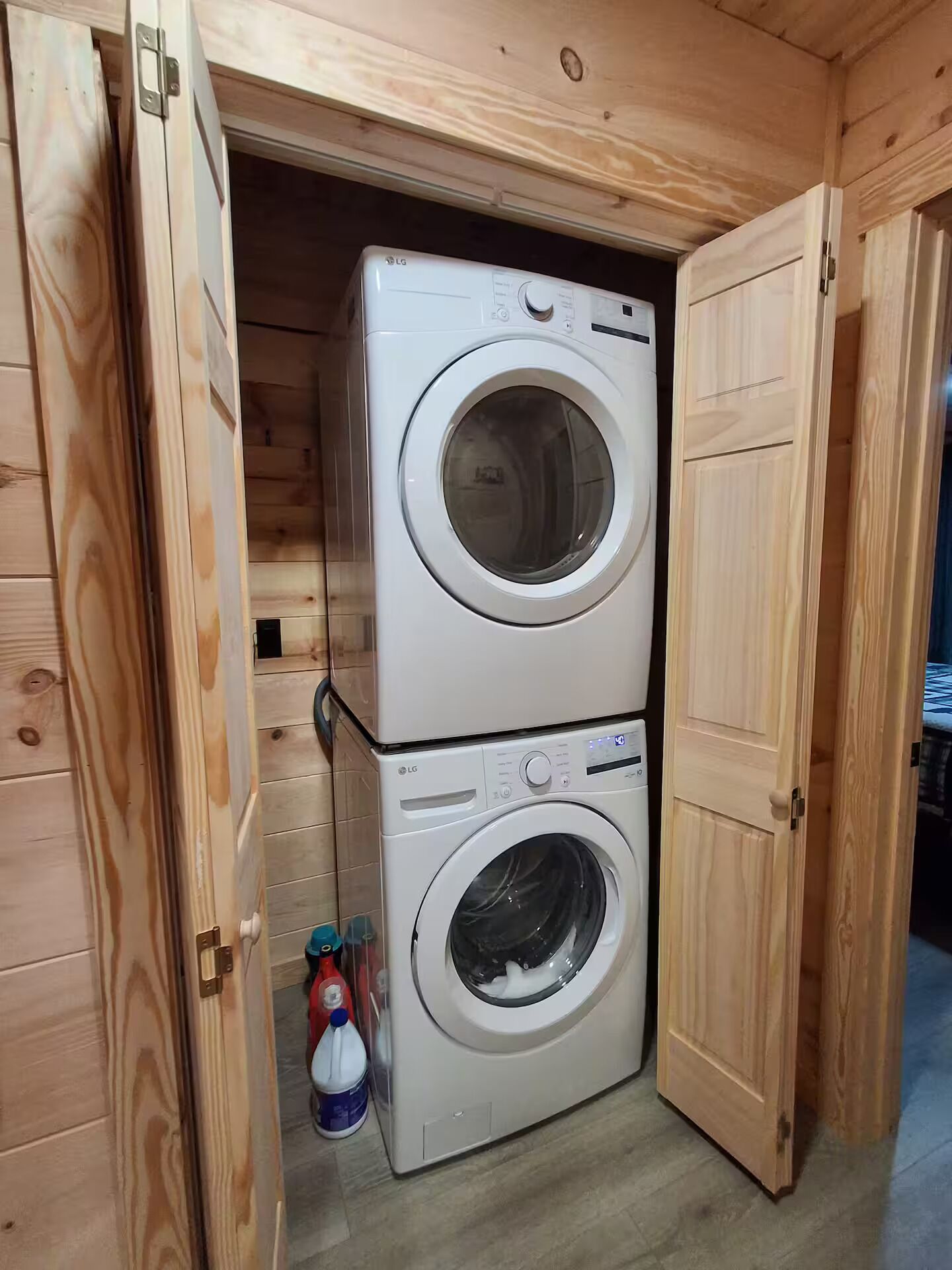A compact laundry room with two stacked washing machines, wooden walls, and a door.