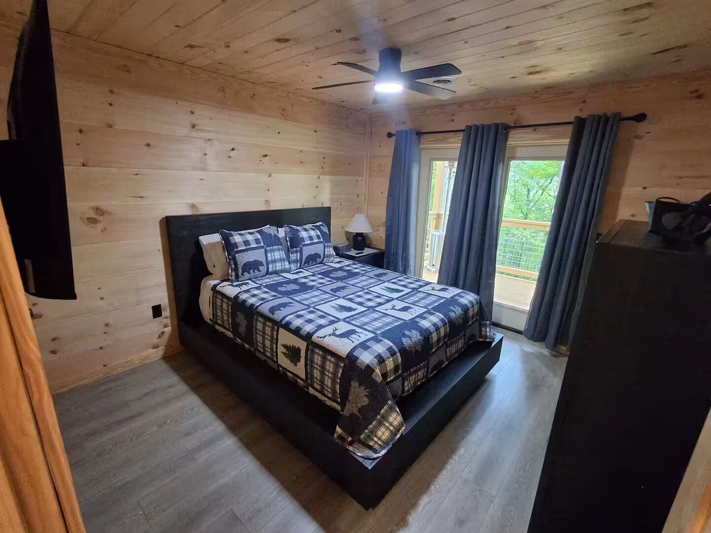Une chambre dans une cabane en bois, avec un lit, un ventilateur de plafond et une fenêtre avec des rideaux.