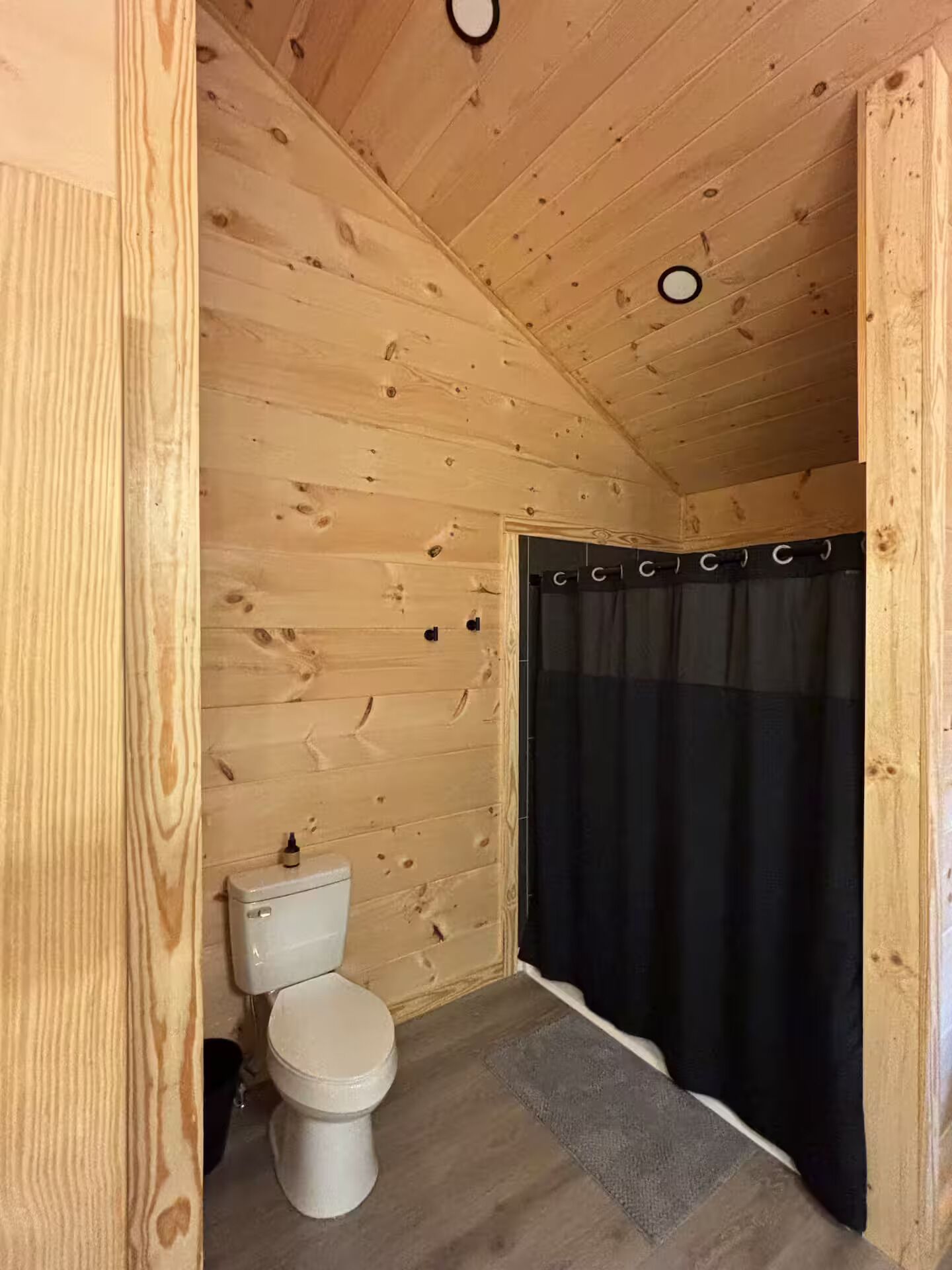 A wooden-paneled bathroom with a toilet and a black shower curtain.