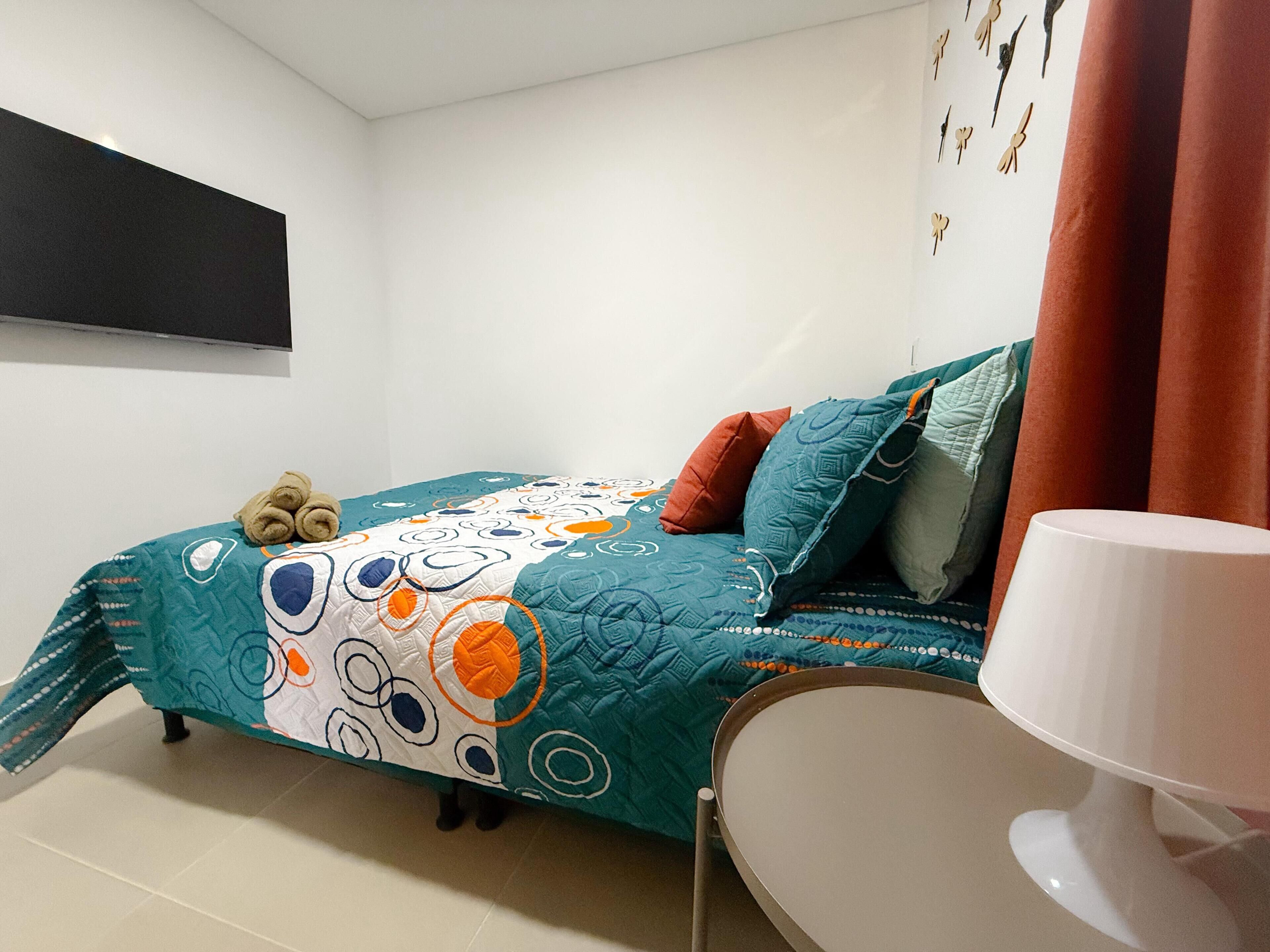 Un dormitorio con cama, almohadas, una lámpara y un reloj de pared.