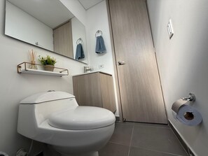 A modern bathroom with a toilet, a sink, a mirror, and a towel rack. - Mountain View, Pool & Gym (2506) (Sabaneta)
