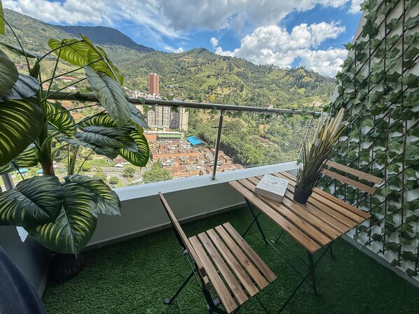 A balcony with a view of a mountainous landscape, a wooden table, and potted plants. - Mountain View, Pool & Gym (2506) (Sabaneta)