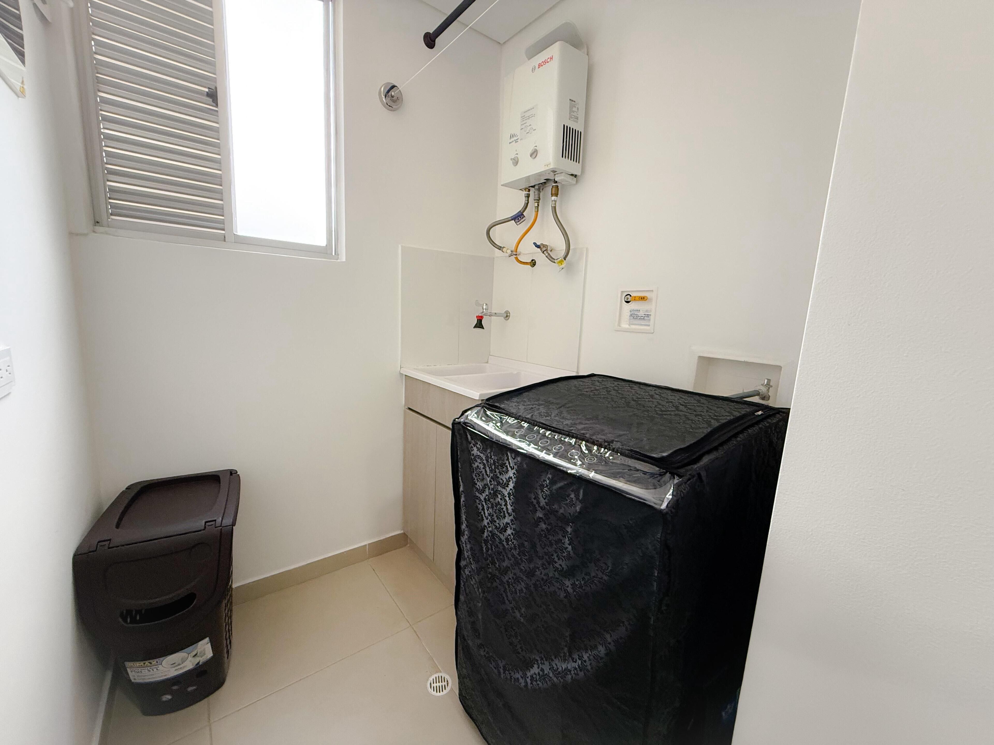 Un baño pequeño y limpio con un calentador de agua Bosch, un lavamanos y un cubo de basura.