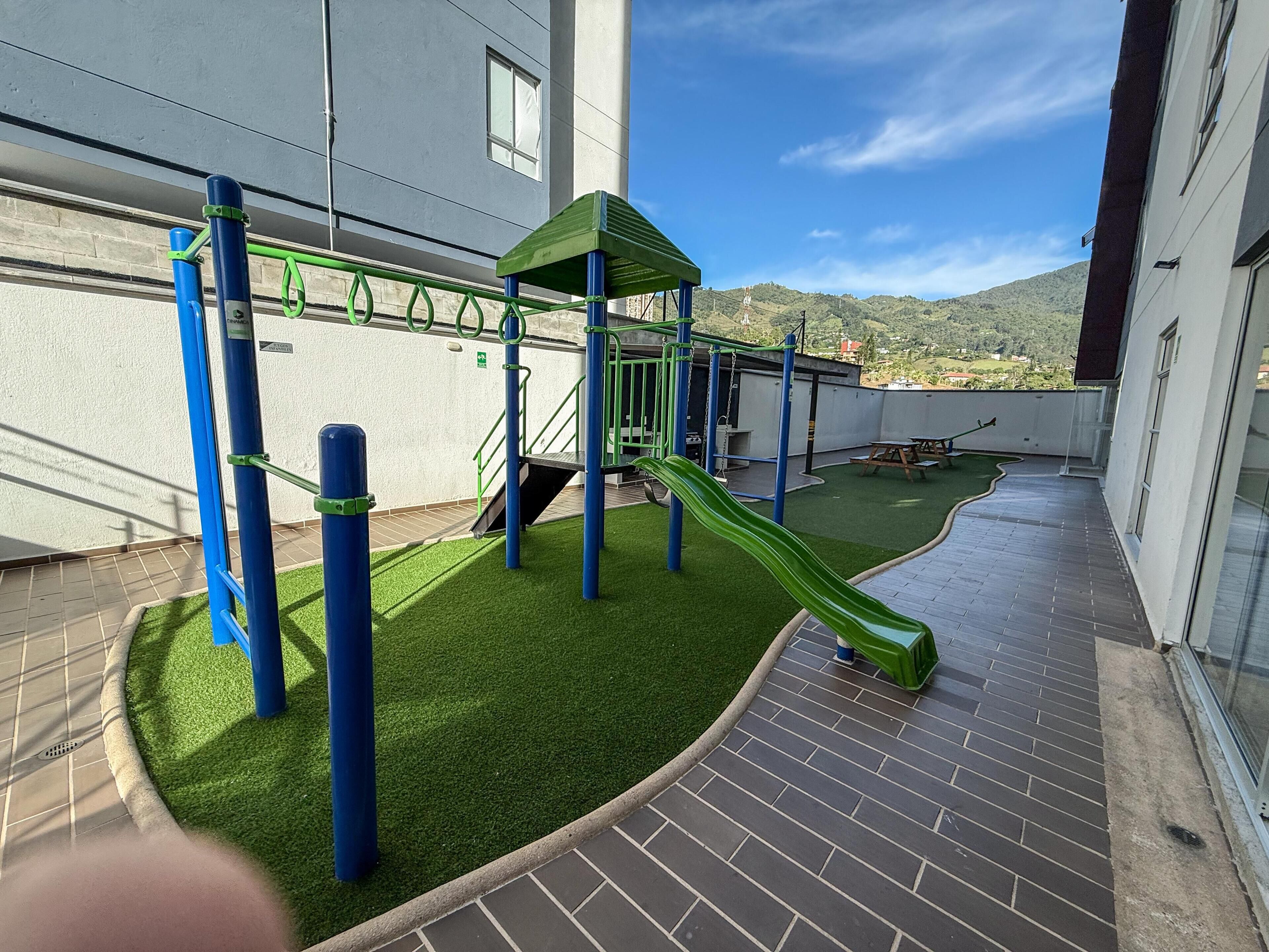 A rooftop playground with a slide, climbing structures, and artificial grass.