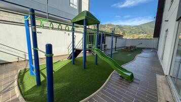 A rooftop playground with a slide, climbing structures, and artificial grass.