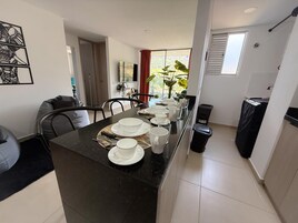 Una cocina moderna con una isla central, mesa de comedor dispuesta con platos, tazas y cubiertos.