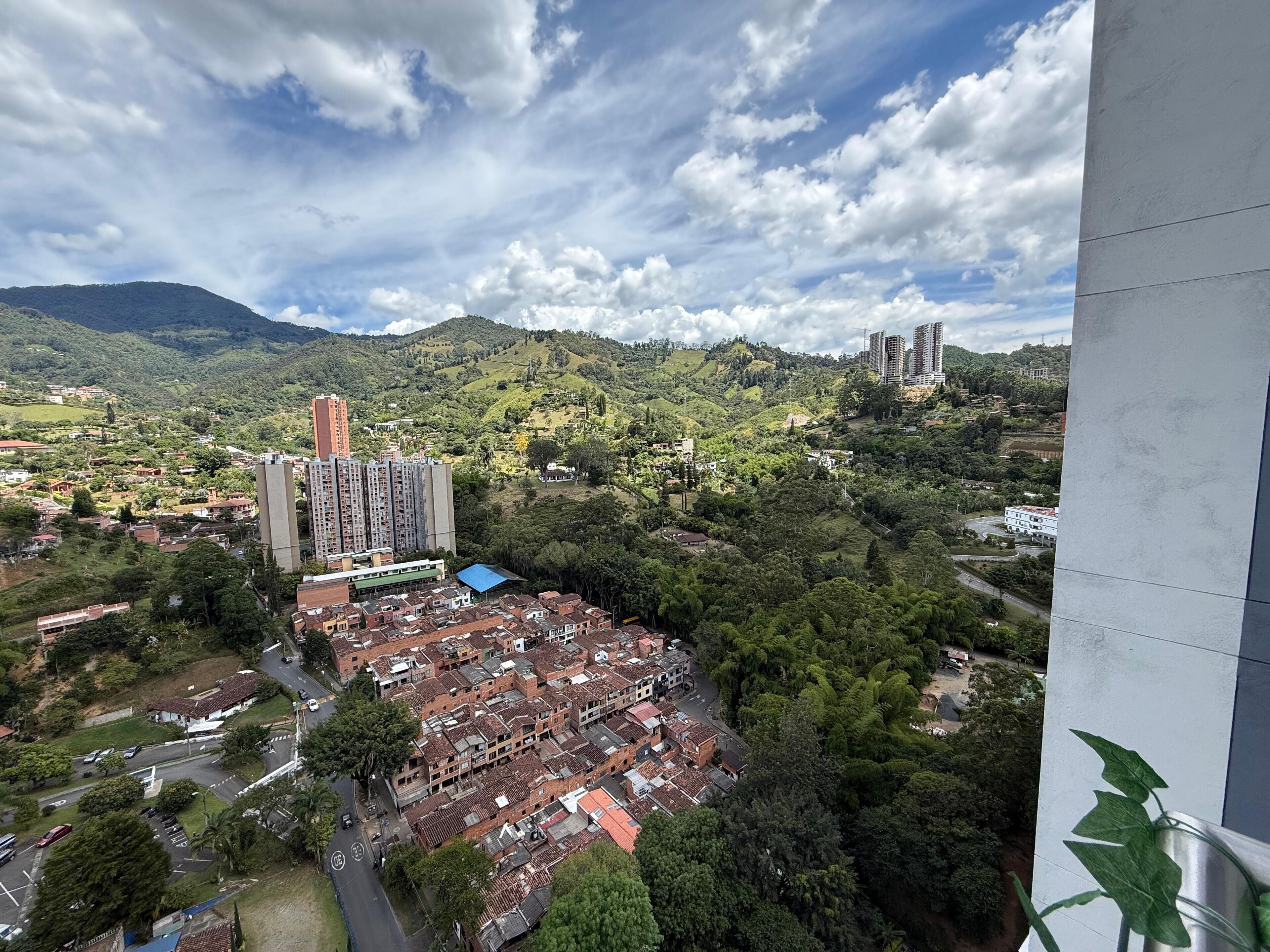 Zona residencial con una combinación de edificios altos y bajos, rodeada de abundante vegetación y colinas.
