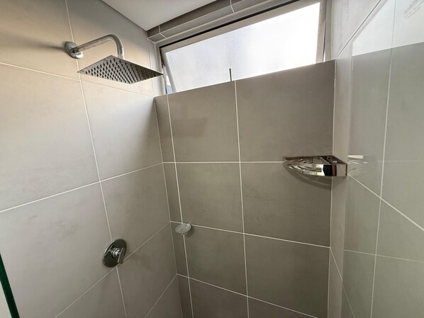 Un espacio con ducha, un cabezal de ducha manual, un grifo de pared y un lavamanos en esquina con jabonera.