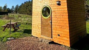 Une petite cabane en bois dotée d’une fenêtre ronde, d’une porte et d’un petit luminaire.