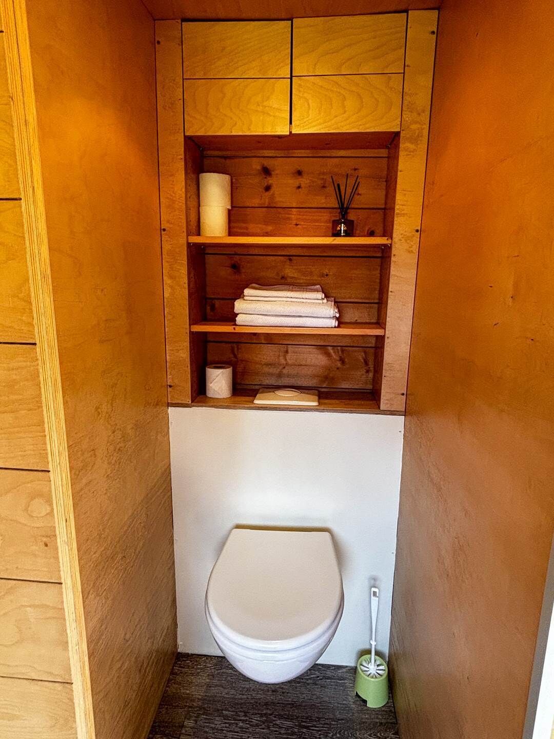Ein kleines Badezimmer mit einem Holzwaschtisch, einer Toilette und einem Regal mit Handtüchern und Pflegeprodukten.