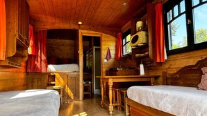 Una cabaña acogedora con dos camas, paredes de madera, una zona de cocina y un ventanal con cortinas.
