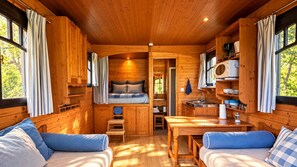 A cozy cabin interior with a bed, a small kitchenette, and a dining area.