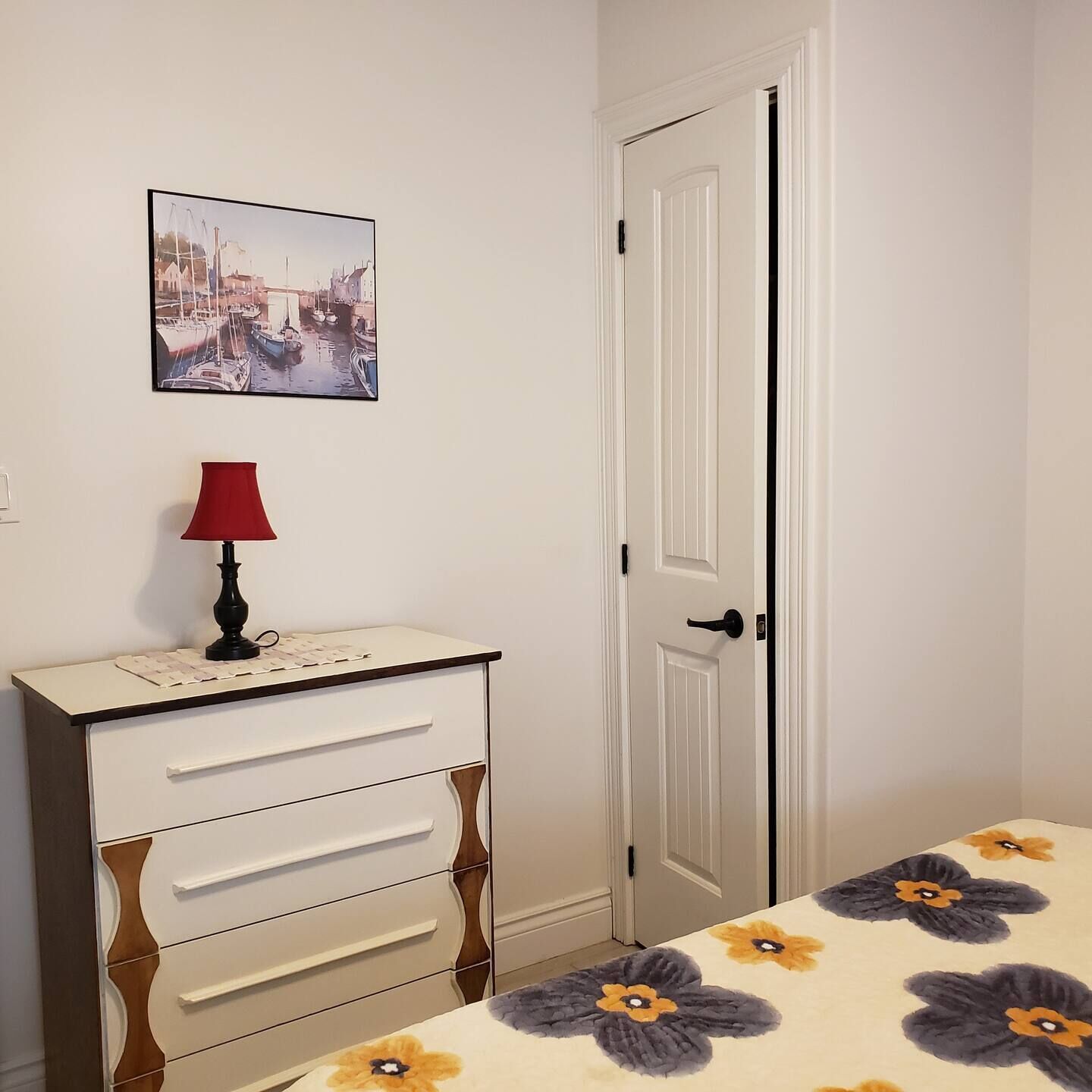 A bedroom with a bed, a nightstand, a lamp, a dresser, and a door.