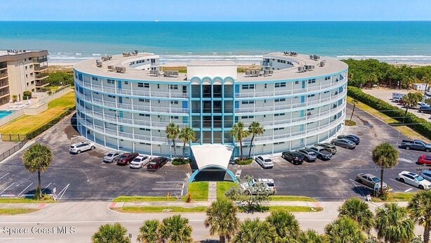 A circular hotel with a central atrium, parking lot, and a view of the ocean. - Sunny Escape 2-Bedroom Condo Steps from Cocoa Beach (Cocoa Beach)