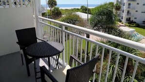 A balcony with a table and chairs, overlooking a beach and a pool. - Sunny Escape 2-Bedroom Condo Steps from Cocoa Beach (Cocoa Beach)