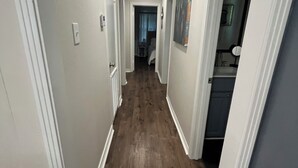 A narrow hallway with wooden flooring, white walls, and a ceiling light.