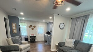 A spacious living room with a dark wood floor, grey sofas, and a ceiling fan.