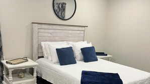 A bedroom with a bed, white nightstands, a round mirror, and a ceiling fan.
