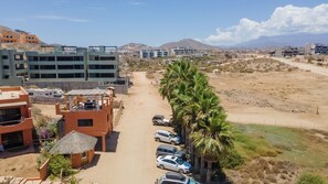 Un hôtel à étages, un parking avec plusieurs voitures et une vue sur le paysage environnant, notamment les montagnes et un ciel dégagé.