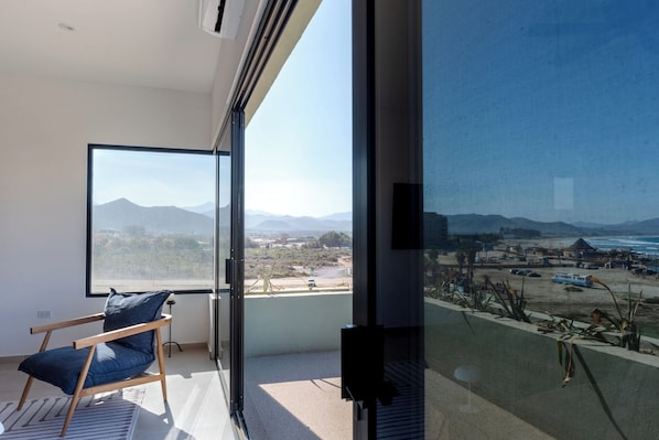 Una habitación moderna con un amplio ventanal que ofrece vistas a la playa y a las montañas.