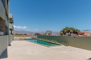 Una piscina en la azotea con vistas despejadas a montañas y un edificio moderno al fondo.