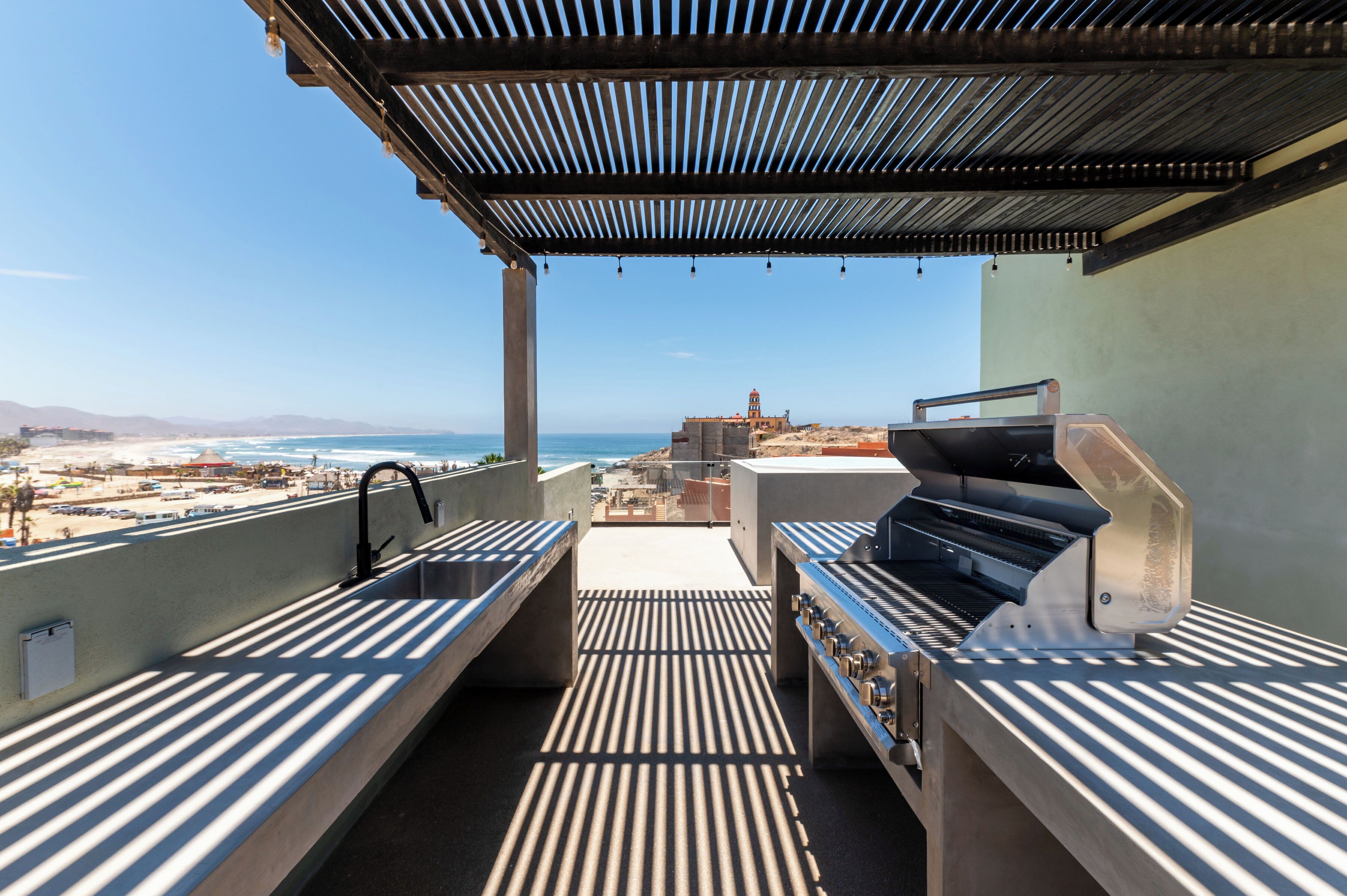 An outdoor patio with a grill and sink, overlooking a beach and ocean view.