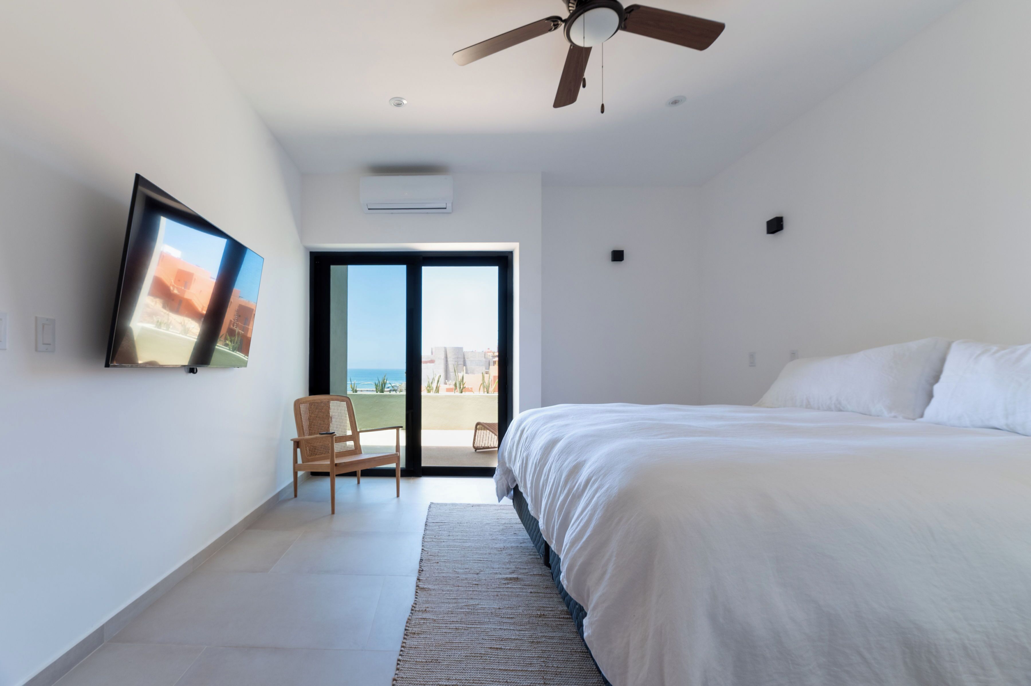 Ett modernt hotellrum med en stor säng, en takfläkt, en platt-TV som är monterad på väggen och utsikt över stranden genom en skjutdörr i glas.