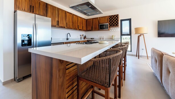 A modern kitchen with wooden cabinets, a stainless steel refrigerator, a microwave, and a large island with bar stools.