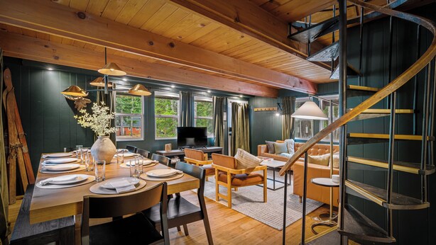 Un comedor con una mesa de madera dispuesta para seis personas, un sofá y una escalera de caracol.