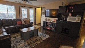 A living room with a dark leather sofa, a wooden coffee table, and a flat-screen TV on a stand. There is a bookshelf with books and a microwave. - Feel cozy and at home! Perfect Location For Exploring! (Provo)