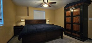 Ein Schlafzimmer mit Bett, Nachttischen, einem Kleiderschrank, einem Deckenventilator und einem Fenster mit Jalousien.
